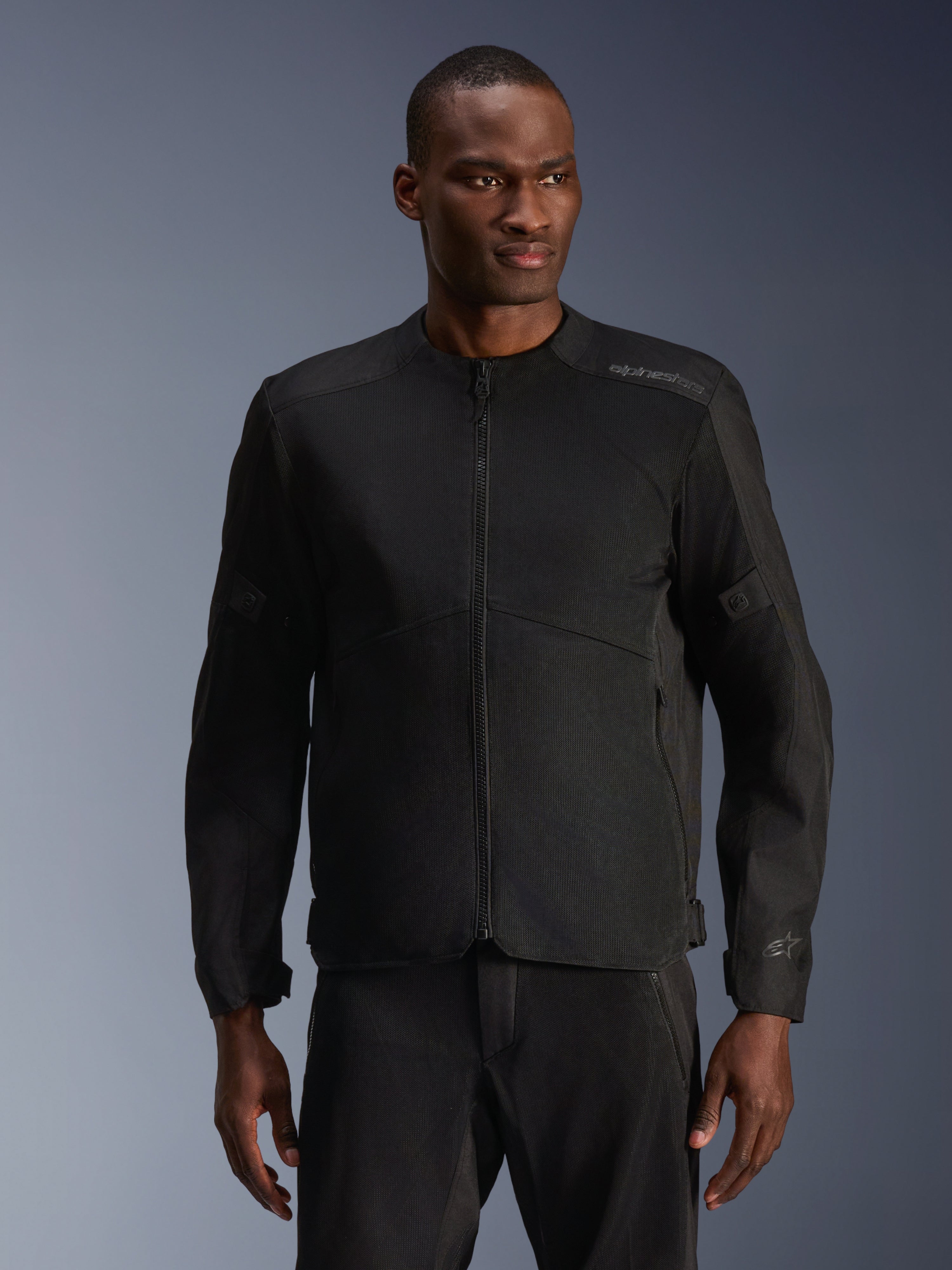 Mandlig model iført Alpinestars C-1 Air-jakke i sort, moderne motorcykeljakke med omfattende tech mesh-paneler og gennemgående lynlås foran, kombineret med matchende sorte kørebukser, æstetik til urban livsstil og pendling