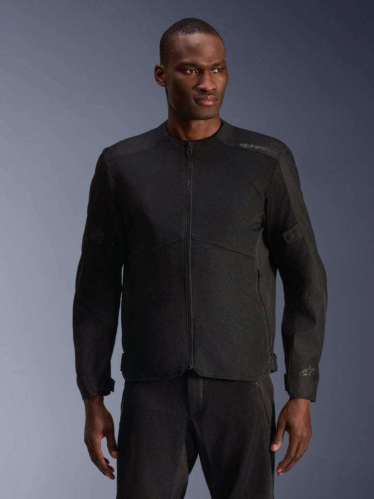 Mandlig model iført Alpinestars C-1 Air-jakke i sort, moderne motorcykeljakke med omfattende tech mesh-paneler og gennemgående lynlås foran, kombineret med matchende sorte kørebukser, æstetik til urban livsstil og pendling