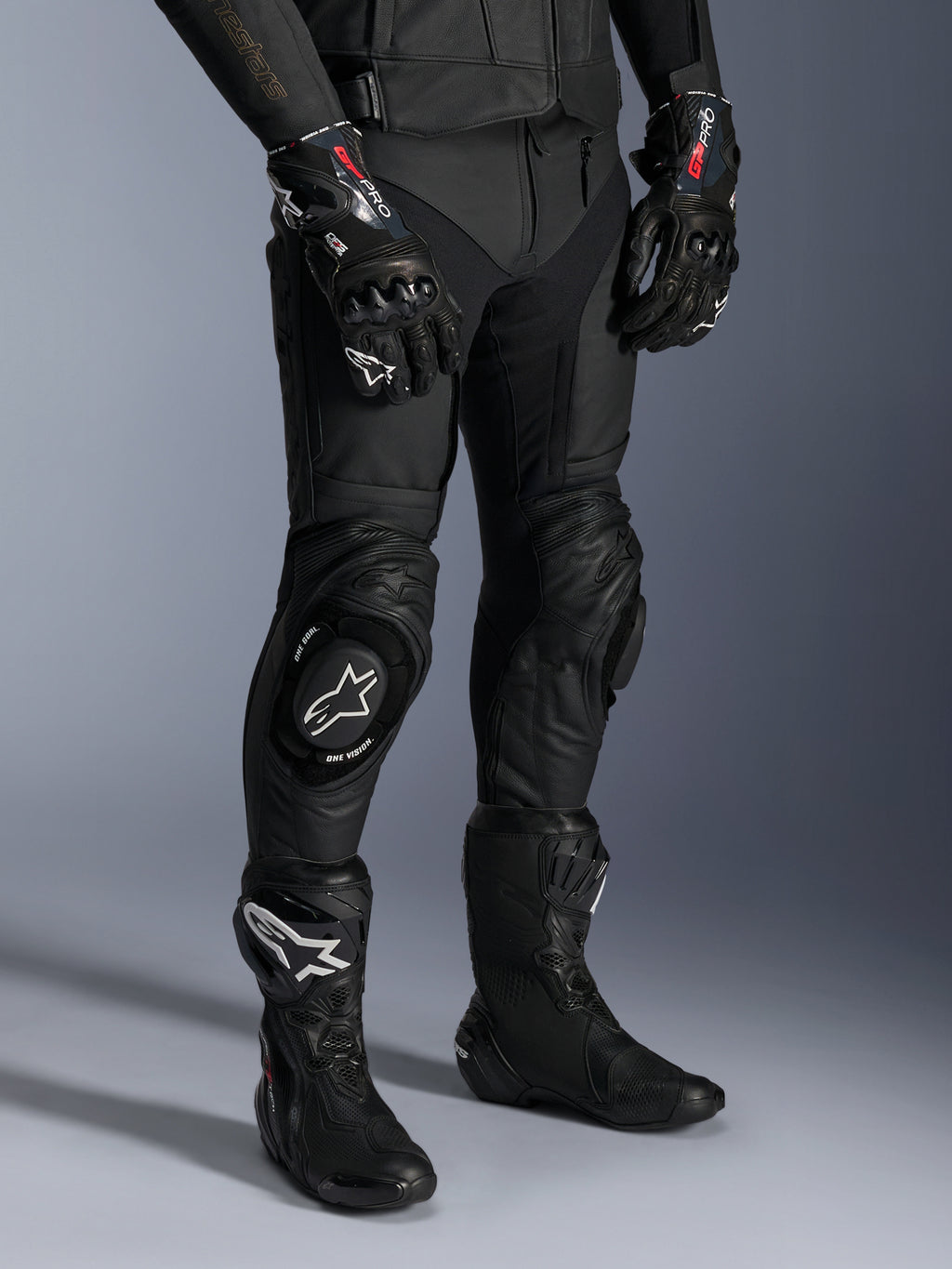 Alpinestars Missile V3 læderbukser, sorte motorcykelracingbukser, båret med matchende GP Pro-handsker og tekniske racingstøvler, premium læderkonstruktion med knæskydere med hvidt logo, professionel racing-æstetik til brug på bane og vej