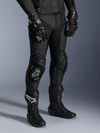 Alpinestars Missile V3 læderbukser, sorte motorcykelracingbukser, båret med matchende GP Pro-handsker og tekniske racingstøvler, premium læderkonstruktion med knæskydere med hvidt logo, professionel racing-æstetik til brug på bane og vej