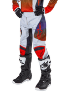 Alpinestars 2024 Youth Racer Hoen bukser, motocross-bukser til unge, lysegrå med Hot Orange og sorte detaljer, røde stjernelogoer på lårene og røde knæpaneler, båret med sort-hvide støvler, holdbart design til off-road kørsel
