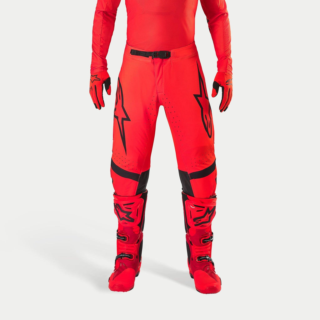 Alpinestars Supertech Ember LE bukser, motocrossbukser, rød fluo og lys rød med sorte detaljer, markante sorte stjernelogoer på lårene, sort taljespænde og knæpaneler, båret med matchende røde støvler og handsker for et koordineret racersæt.