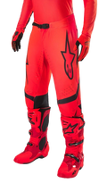 Alpinestars Supertech Ember LE Motocross Pants, Red Fluo and Bright Red with Black accents, worn with matching red racing boots and gloves, featuring a prominent black star logo on the leg, secure waist buckle, and perforated zones for ventilation.