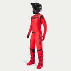 Motocross-kører iført komplet racerudstyr, Supertech Ember LE trøje og bukser i Red Fluo og sort, sort hjelm med goggles, matchende røde og sorte støvler og handsker, koordineret professionelt outfit til terrænkørsel