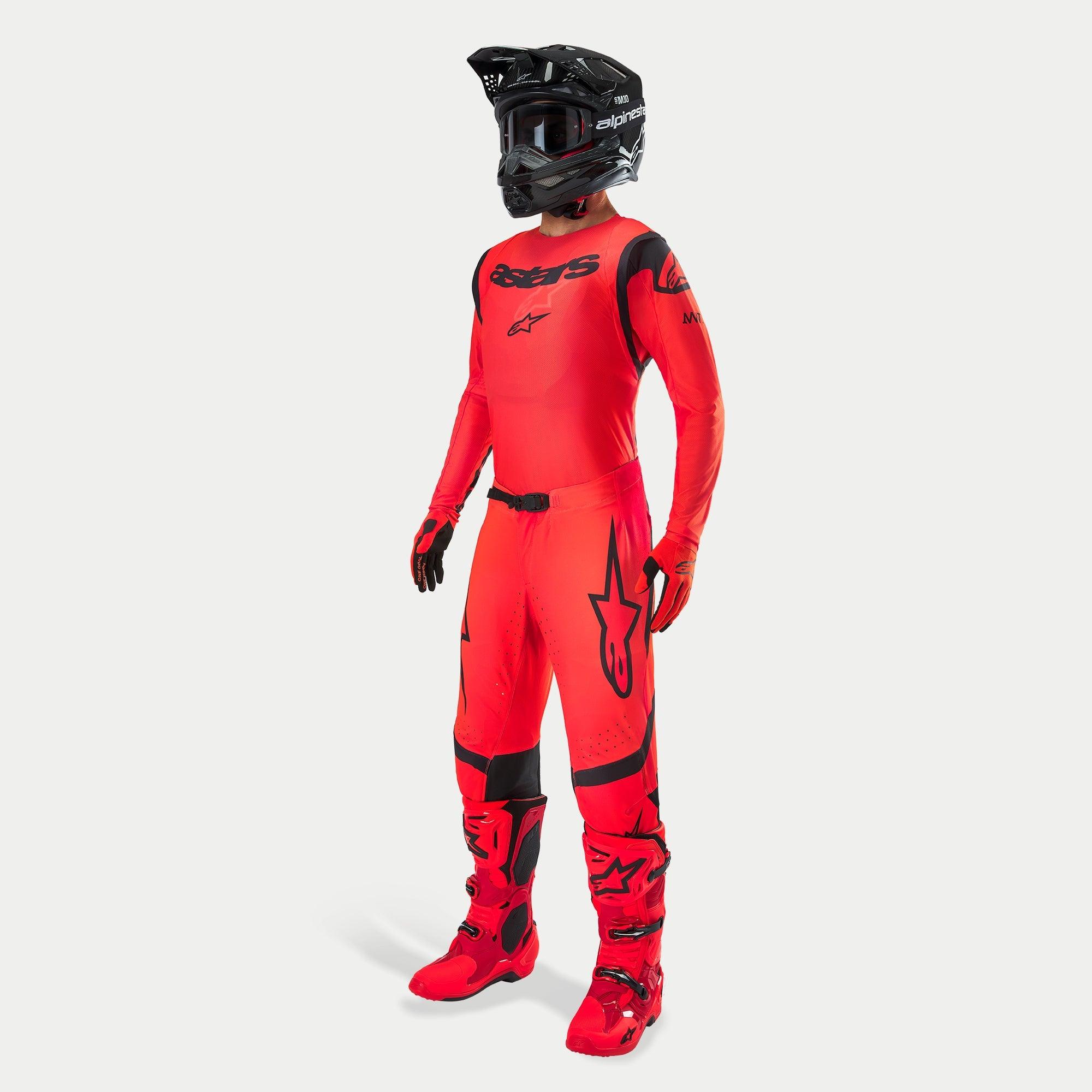 Motocross-kører iført komplet racerudstyr, Supertech Ember LE trøje og bukser i Red Fluo og sort, sort hjelm med goggles, matchende røde og sorte støvler og handsker, koordineret professionelt outfit til terrænkørsel