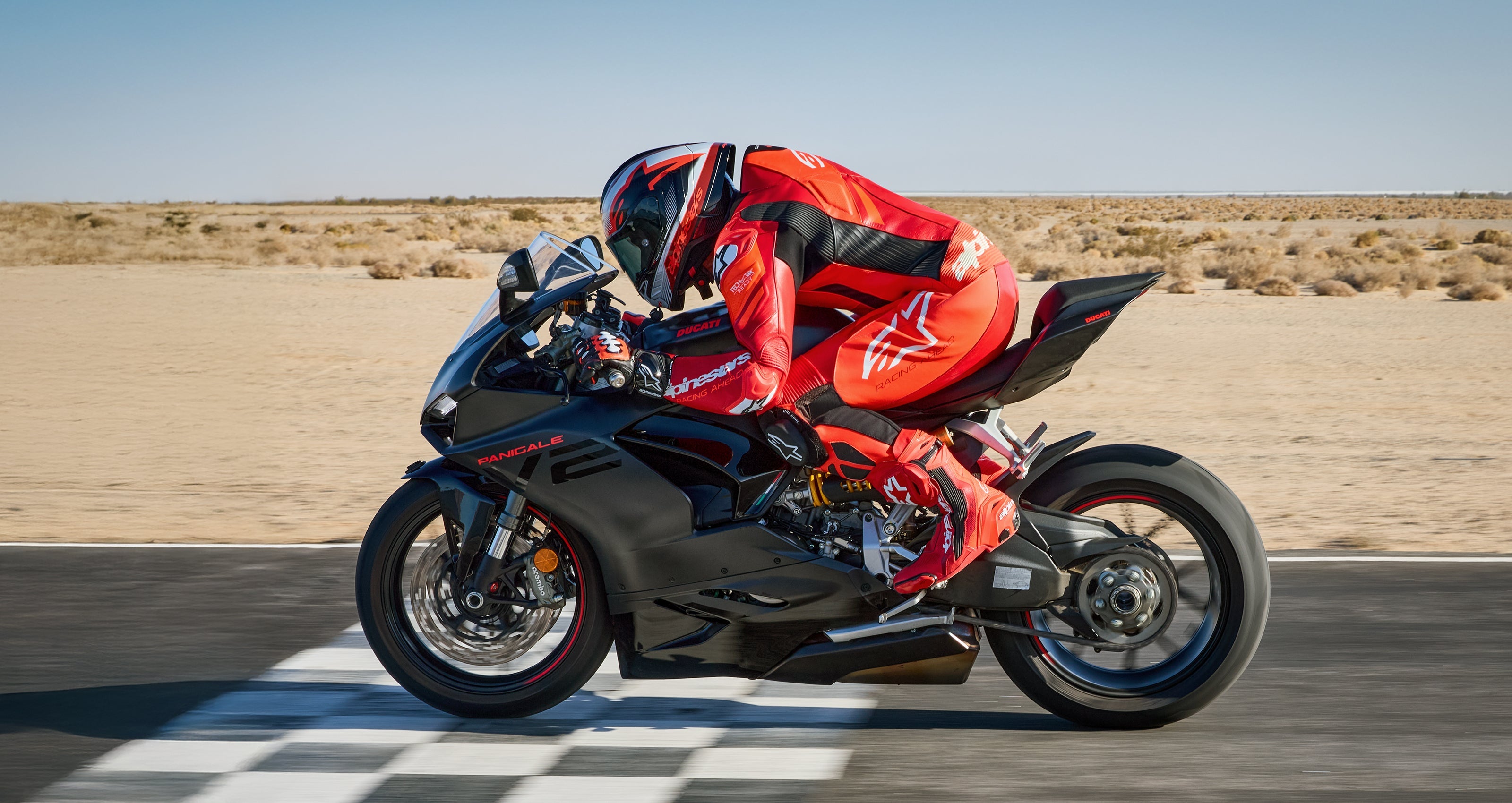 Alpinestars GP Plus V4 Sprint 1PC Leather Suit in Red and White, worn by a rider in a tucked racing position on a track.